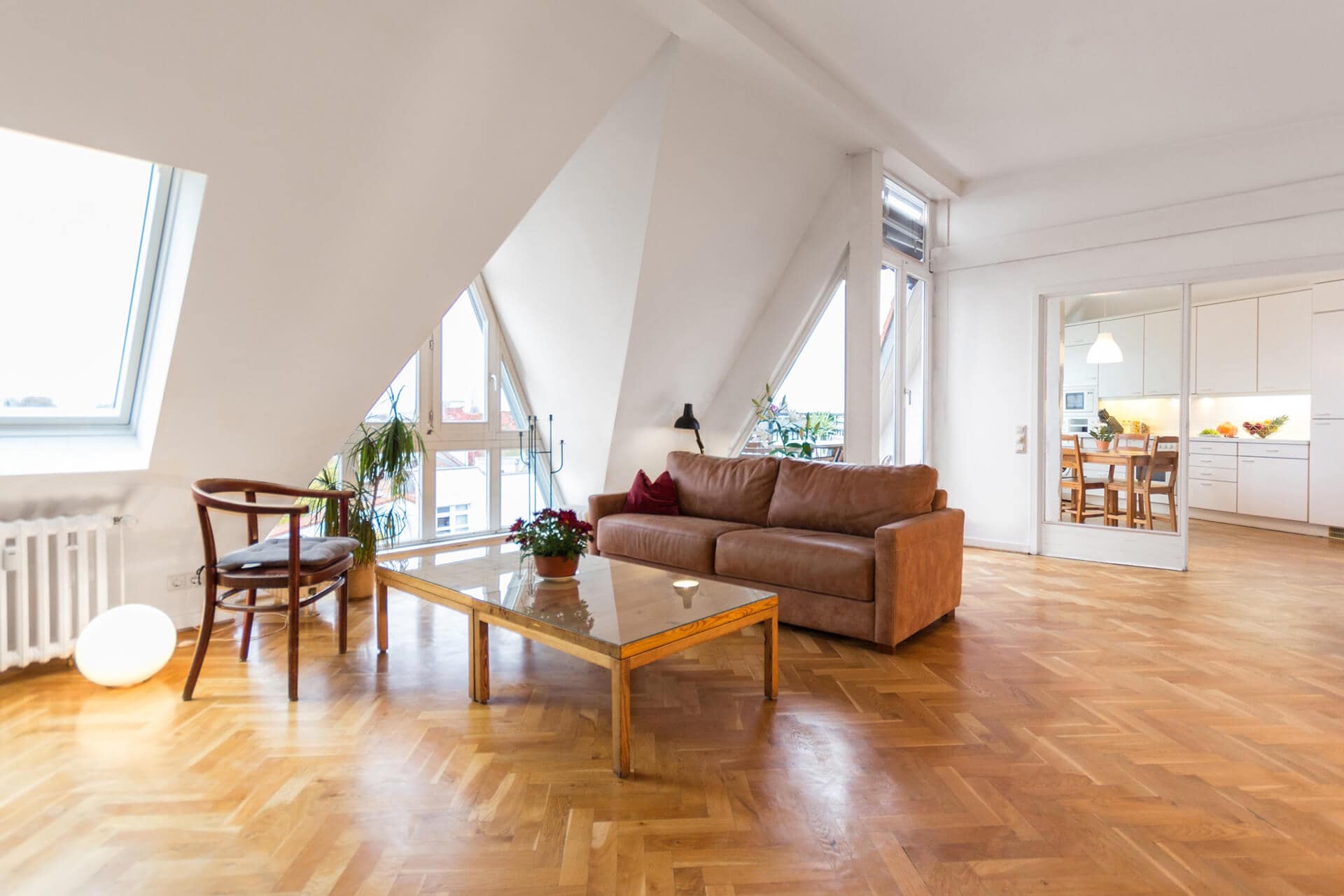 Bright living room with sloped ceiling, large windows, and wooden flooring.