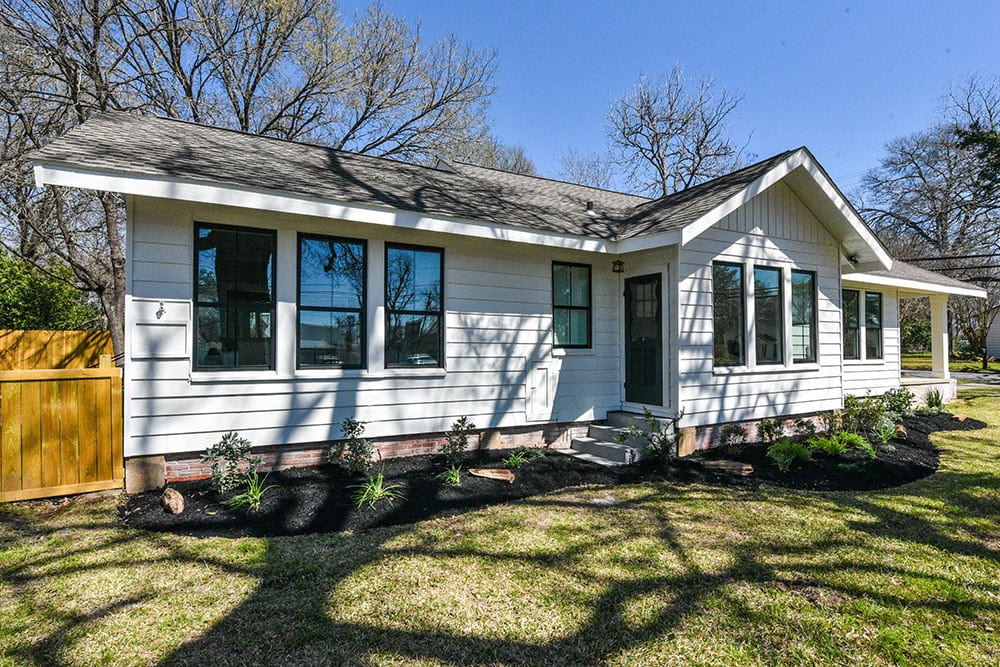 Newly built white house with large windows and a front porch in a residential neighborhood.