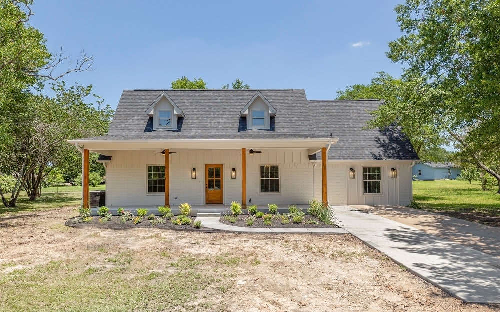 Newly built white house with front porch and dormer windows in a rural area.